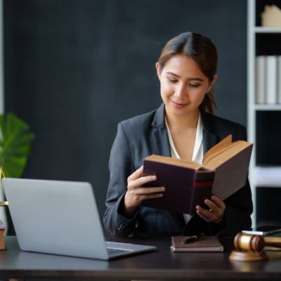 kobieta prawnik siedzi przy biurku, na którym jest otwarty laptop i czyta książkę